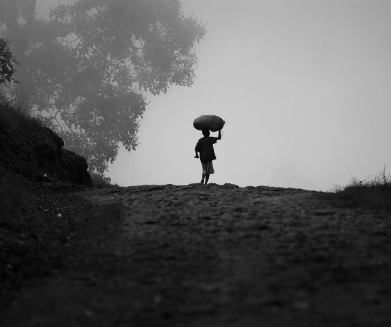 foto en blanco en negro de un niño subiendo una cuesta con un cesto en la cabeza